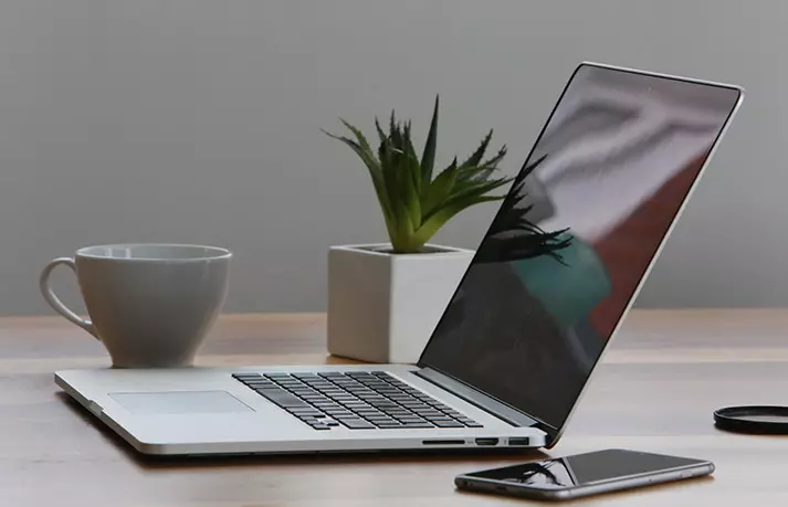 A laptop and an iPhone placed on a table, illustrating the benefits of choosing refurbished devices for savings and sustainability.