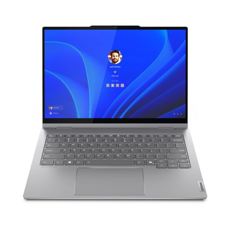 A sleek Lenovo ThinkBook 14-IML sits open, showcasing a silver design with a login screen featuring a user icon and name, all set against a calming blue abstract wallpaper. The keyboard is prominently visible as you view the laptop from the front.