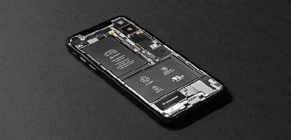 A refurbished iPhone with its back cover removed reveals internal components like the battery, circuit boards, and connectors. The device, displayed diagonally on a matte black surface, highlights the importance of battery health in ensuring optimal performance.