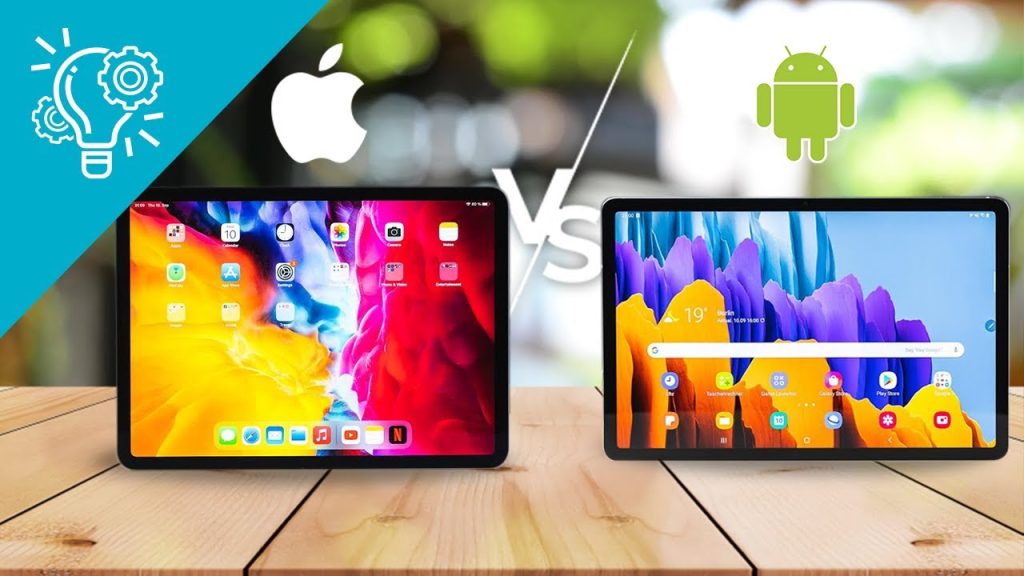 Two tablets rest on a wooden table: one shows an Apple iPad home screen, the other an Android tablet. Large Apple and Android logos with a VS symbol highlight the Apple iPad Vs Android Tablets comparison in the background.
