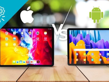 Two tablets rest on a wooden table: one shows an Apple iPad home screen, the other an Android tablet. Large Apple and Android logos with a VS symbol highlight the Apple iPad Vs Android Tablets comparison in the background.