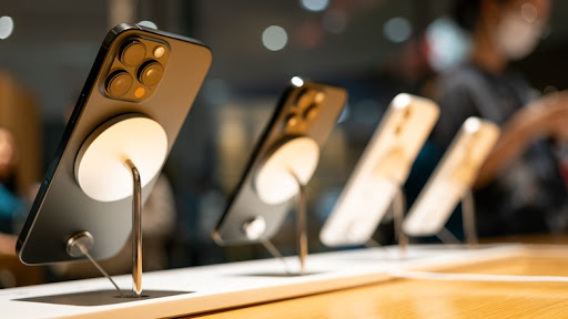 Three smartphones displayed on stands in a modern retail store, showcasing their sleek designs and camera features.