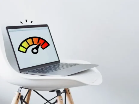 A laptop on a white chair displays a colorful speedometer graphic indicating performance levels.