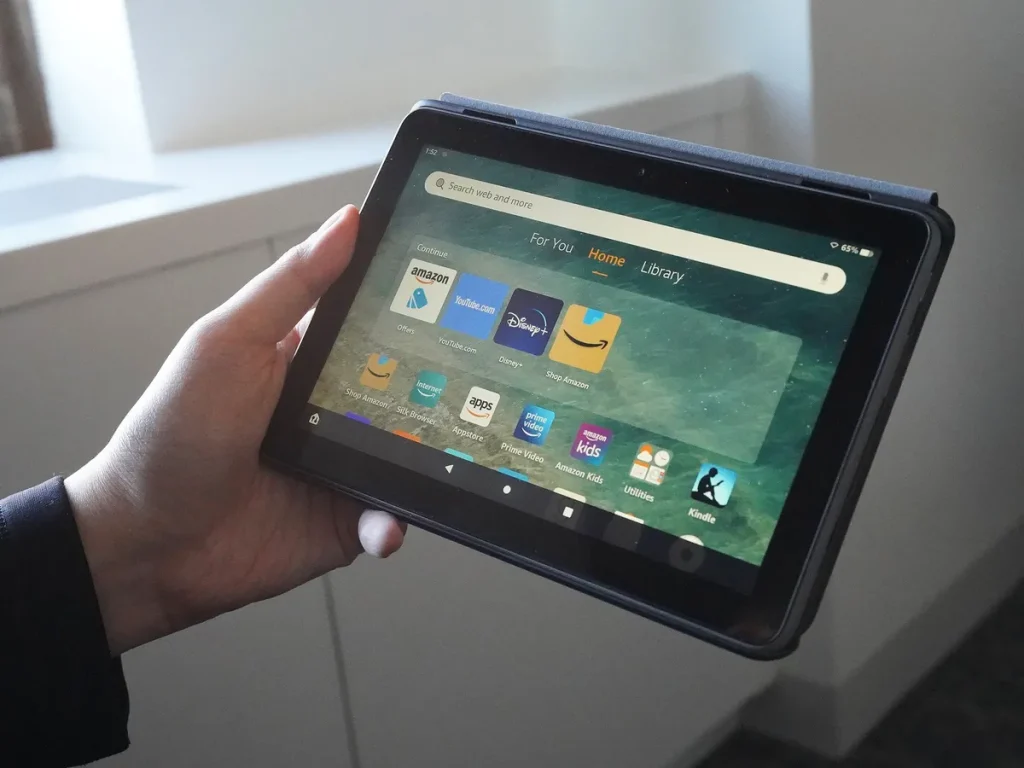 A person holds a tablet displaying various app icons including Amazon, YouTube, and Disney+, with a serene background.