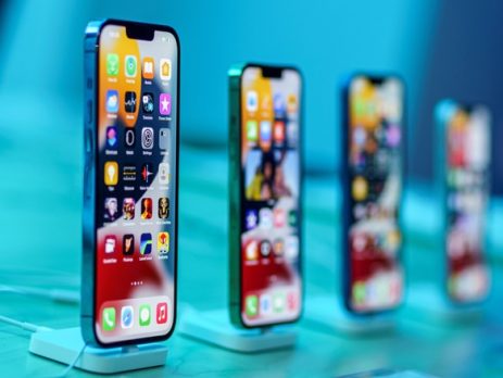 Four smartphones are displayed upright on stands, each showing colorful home screens with various app icons, against a blue-toned background.