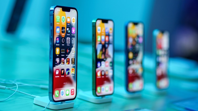 Four smartphones are displayed upright on stands, each showing colorful home screens with various app icons, against a blue-toned background.