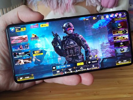 A hand holding a smartphone displaying a gaming interface with a soldier character, featuring various game modes and events.