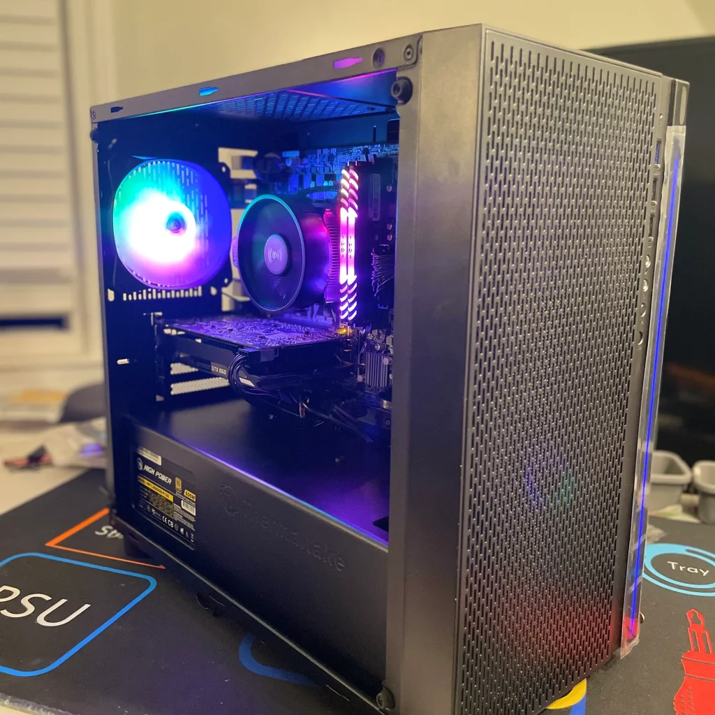 A gaming PC with RGB lighting is displayed on a desk. Its illuminated fans and RAM sticks are visible through the side panel. The mesh front enhances airflow, making it a standout among Top Refurbished PCs for Every Budget in 2025.