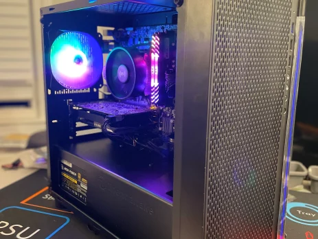 A gaming PC with RGB lighting is displayed on a desk. Its illuminated fans and RAM sticks are visible through the side panel. The mesh front enhances airflow, making it a standout among Top Refurbished PCs for Every Budget in 2025.