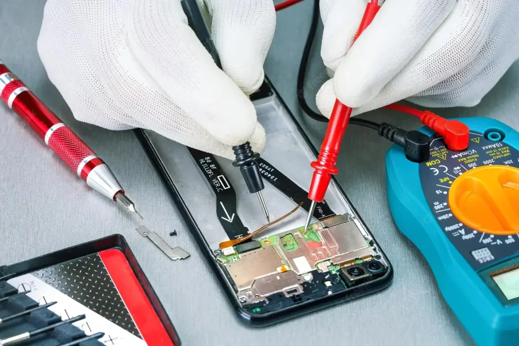A person wearing white gloves uses probes to test the circuitry inside an open smartphone, showcasing the precision and care that highlight why you should choose Creative IT for phone repairs. A screwdriver, small parts, and a digital multimeter are nearby on the work surface.