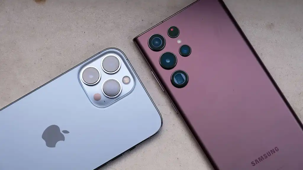 A close-up of the back of an Apple iPhone and a Samsung Galaxy smartphone, showing the camera modules and brand logos on a light surface—perfect for those debating iPhone vs Samsung: which one is better?.